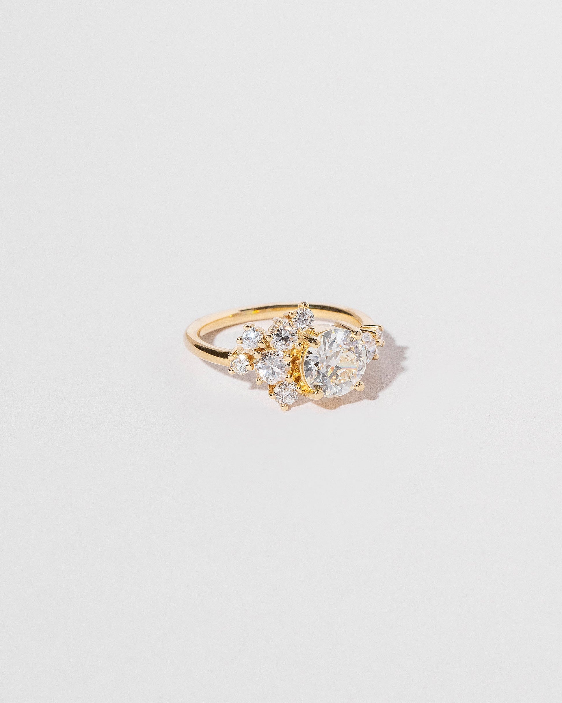 Cluster style ring with white diamonds set in 18k yellow gold, left side close up on light color background.