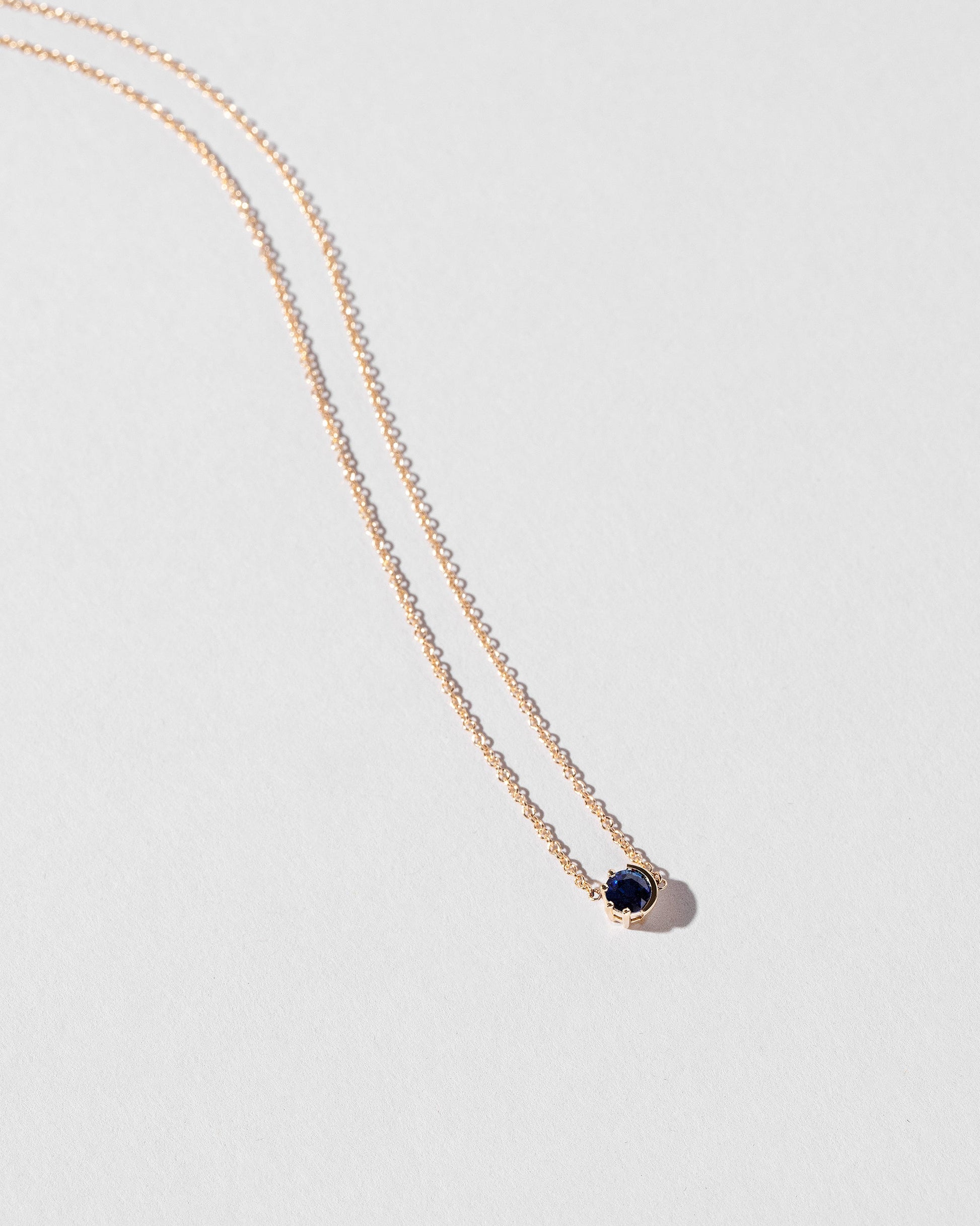 Closeup view of the Sapphire Sun & Moon Necklace on light color background.