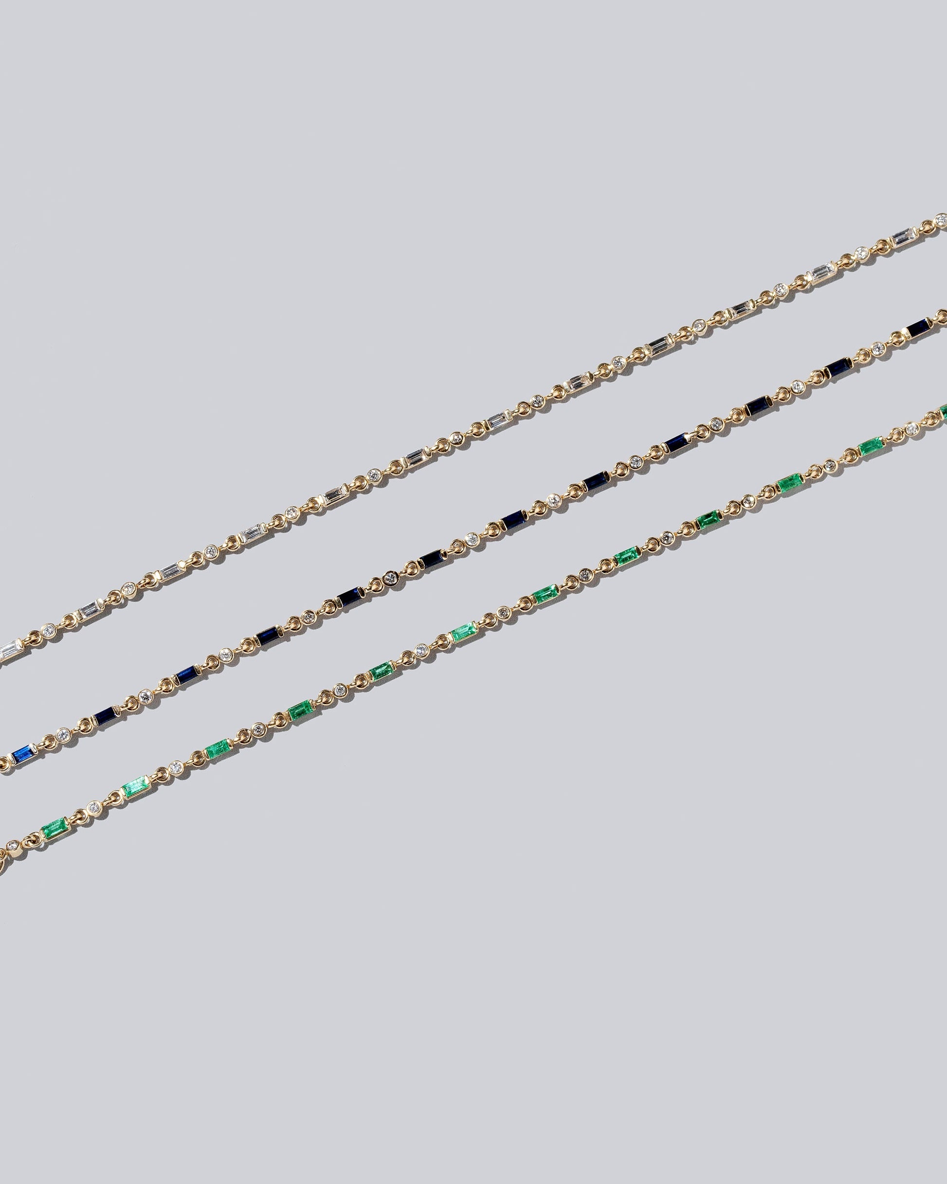 Group of White Diamond, Blue Sapphire and Emerald Full Building Blocks Bracelets on light color background.
