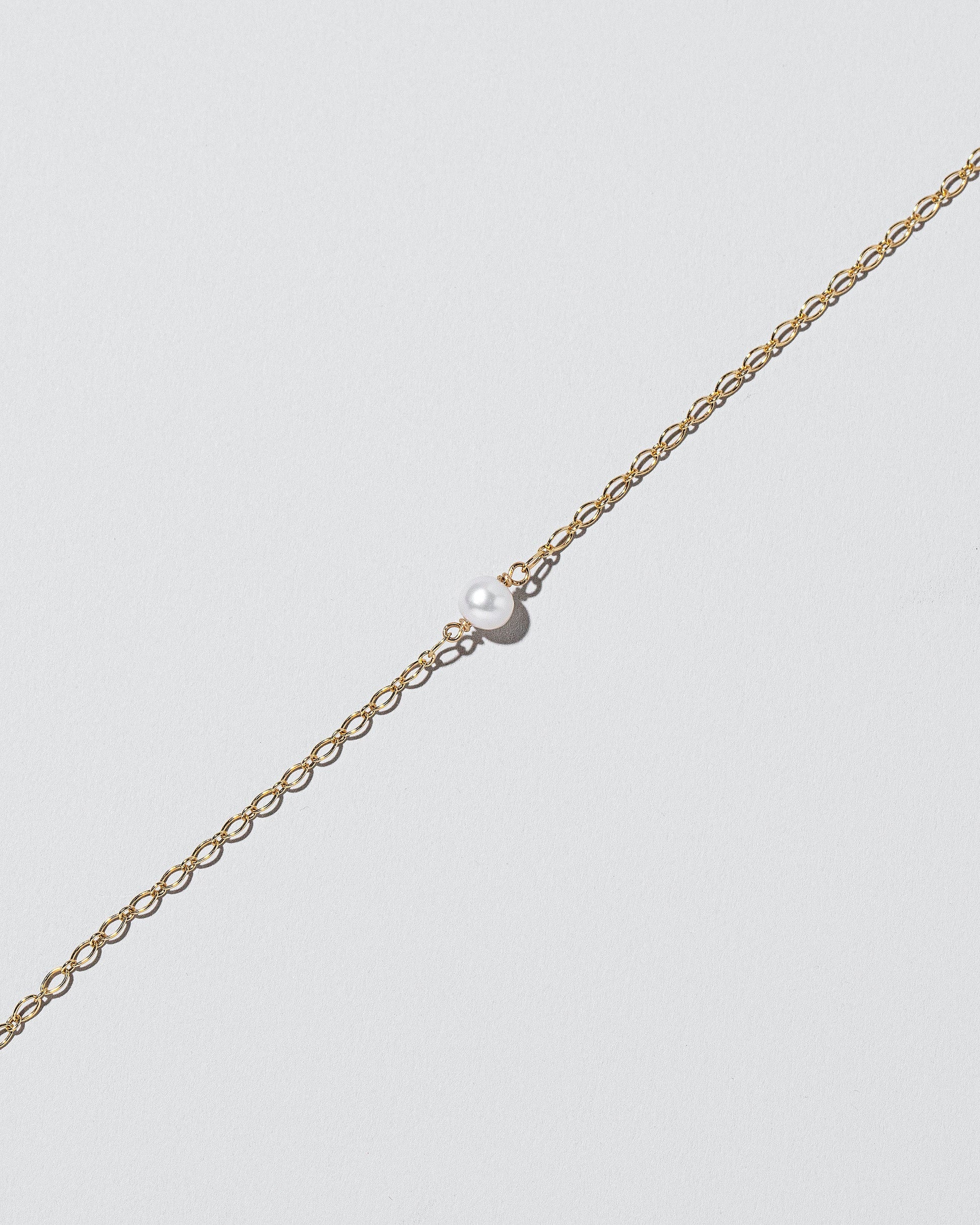 Closeup details of the One Pearl Station Bracelet Open Oval Chain on light color background.