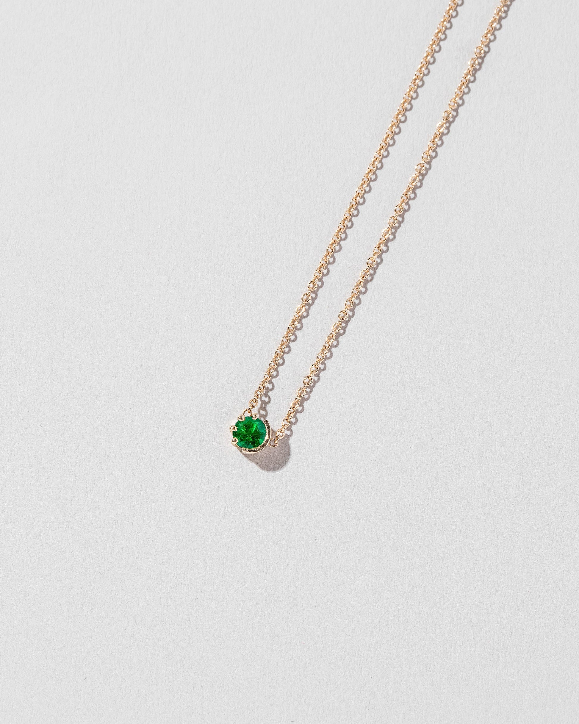 Closeup detail of the Emerald Sun & Moon Necklace on light color background