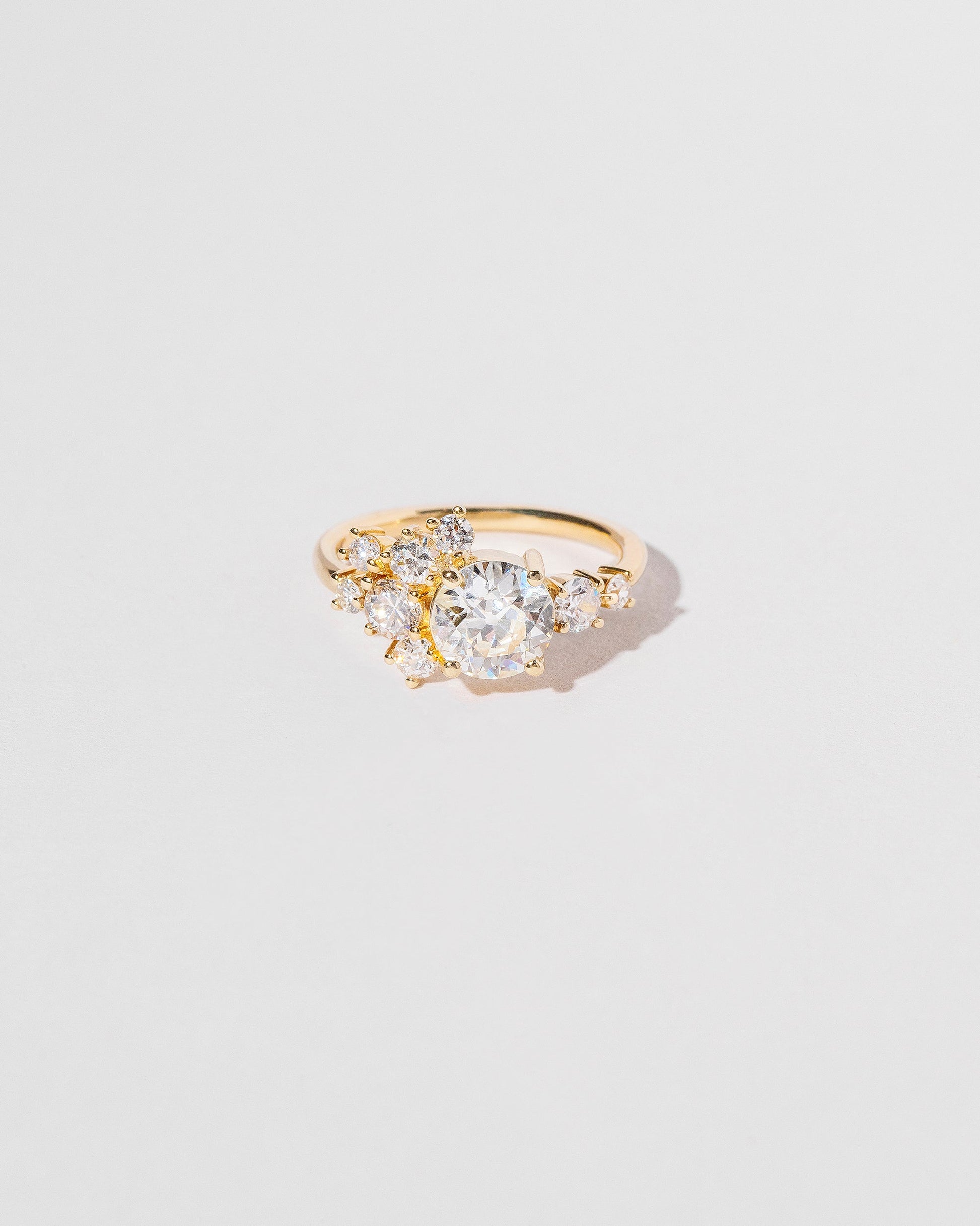 Cluster style ring with white diamonds set in 18k yellow gold, close up on light color background.