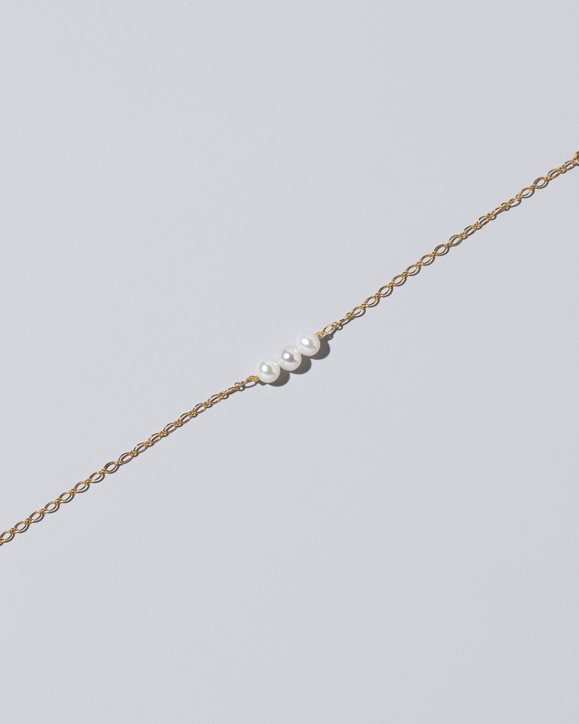 Closeup details of the Three Pearl Station Bracelet Open Oval Chain on light color background.