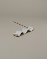 In-use detail view of the Rachel Saunders Glossy White Wave Incense Holder on light color background.