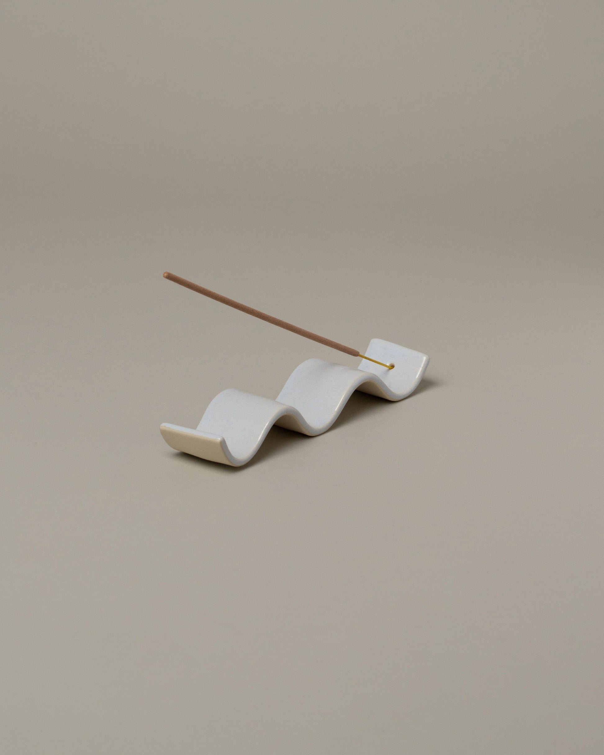 In-use detail view of the Rachel Saunders Glossy White Wave Incense Holder on light color background.
