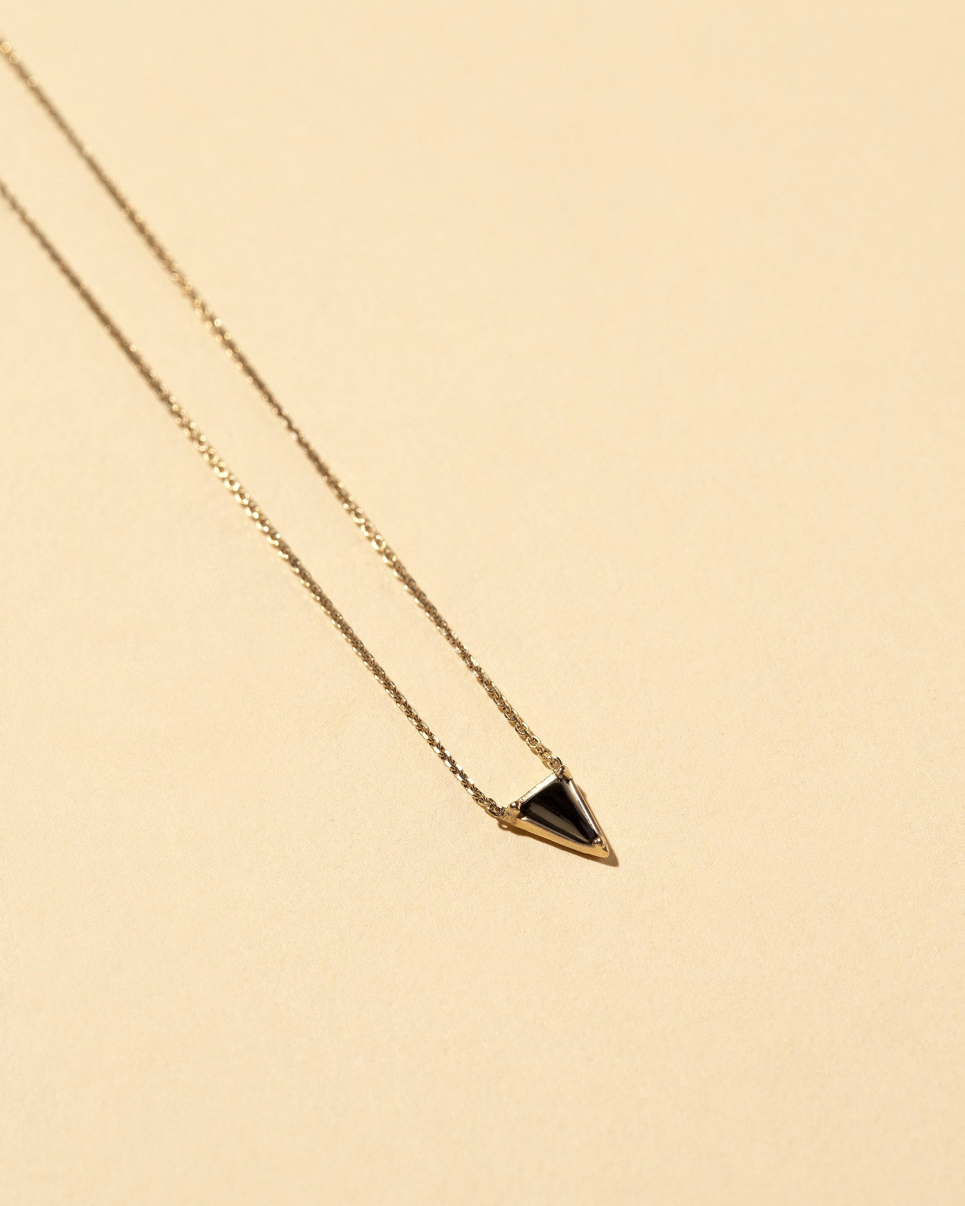 Closeup details of the Gold Black Spinel Triangle Necklace on light color background.