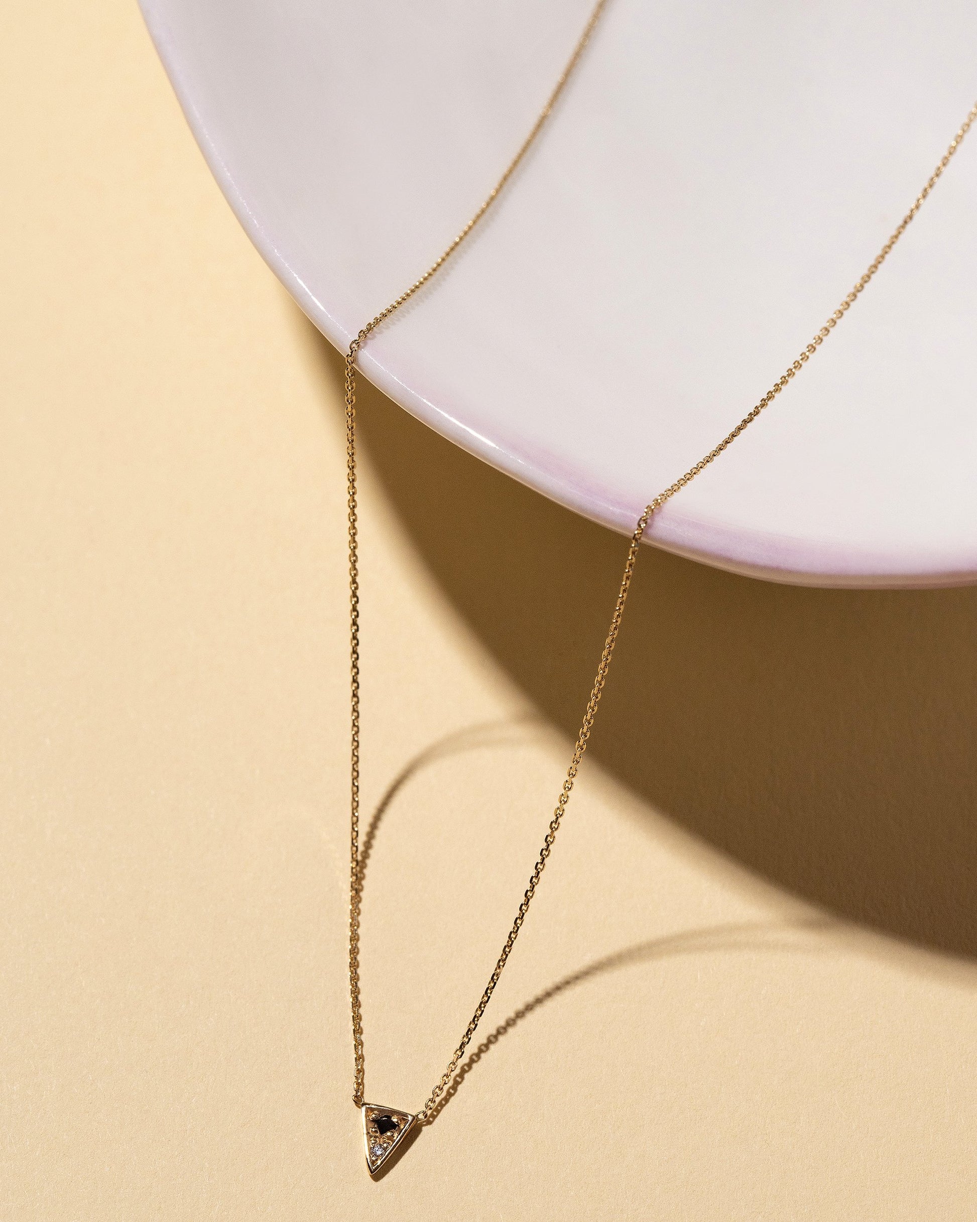 Closeup details of the Gold Black & White Diamond Triangle Necklace on light color background.