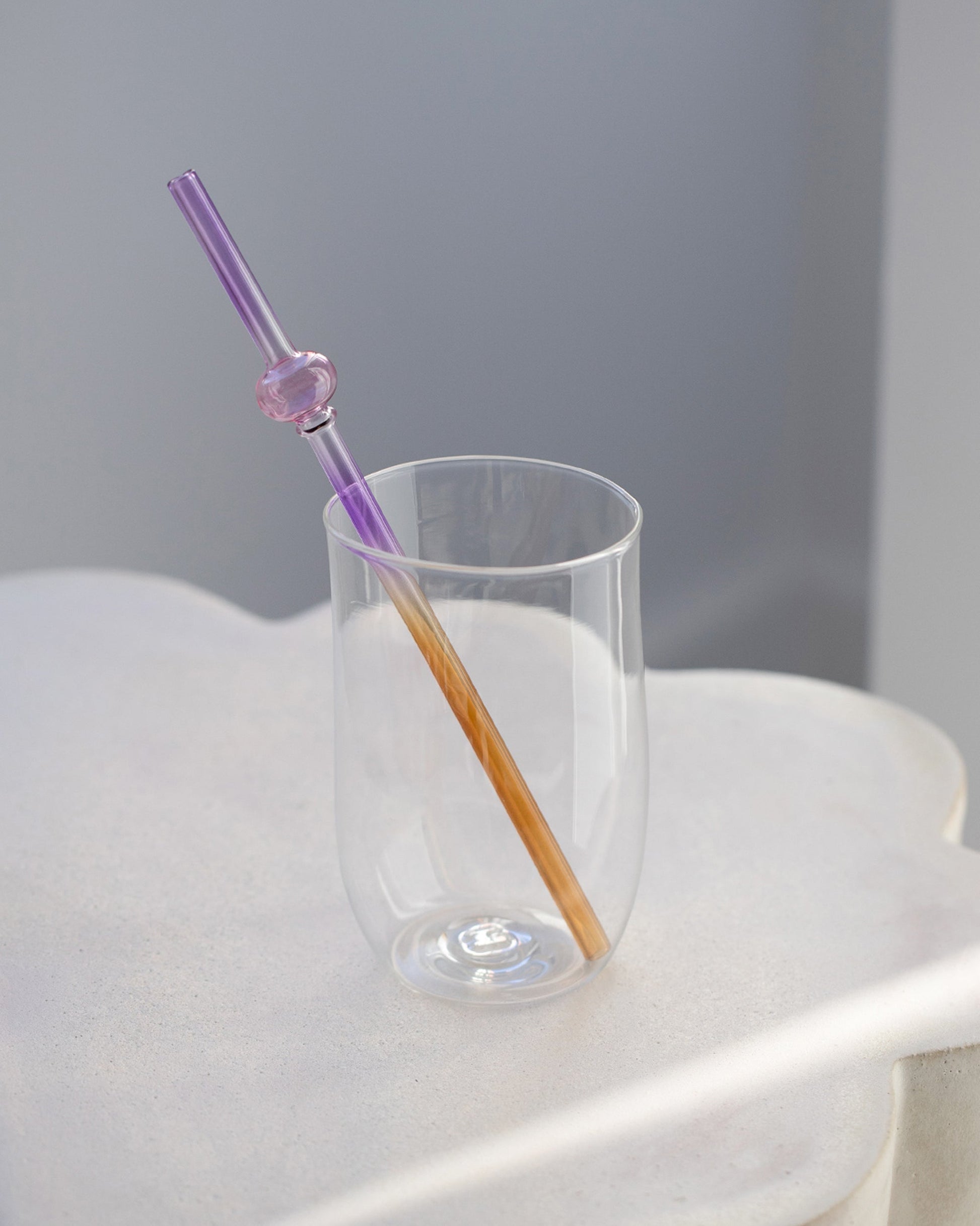 Styled image featuring Misha Kahn Purple and Orange Suck It Up Glass Straw and Ichendorf Milando White Long Drink Glass.
