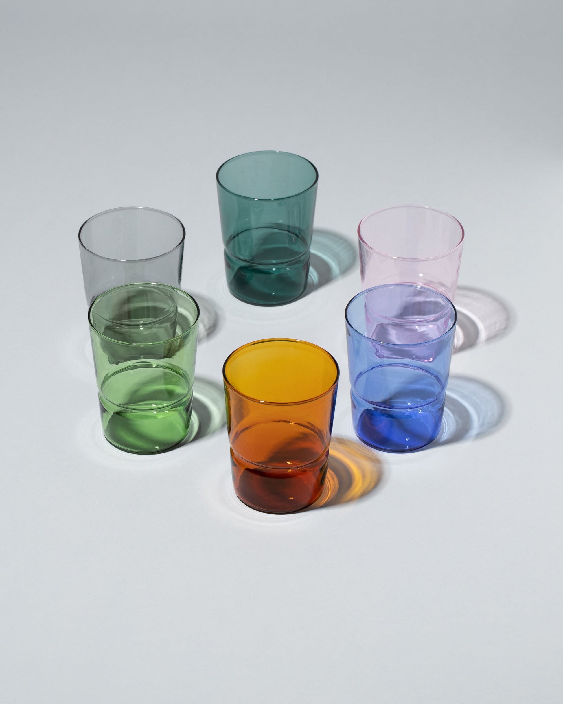 Group of Ichendorf Milano Green, Light Blue, Pink, Smoke, Teal and Amber TAP Glasses on light color background.