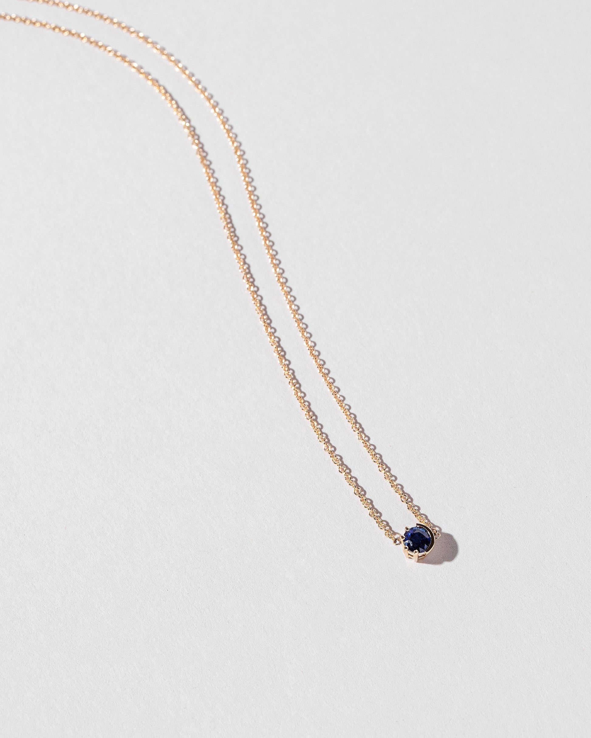 Closeup view of the Sapphire Sun & Moon Necklace on light color background.