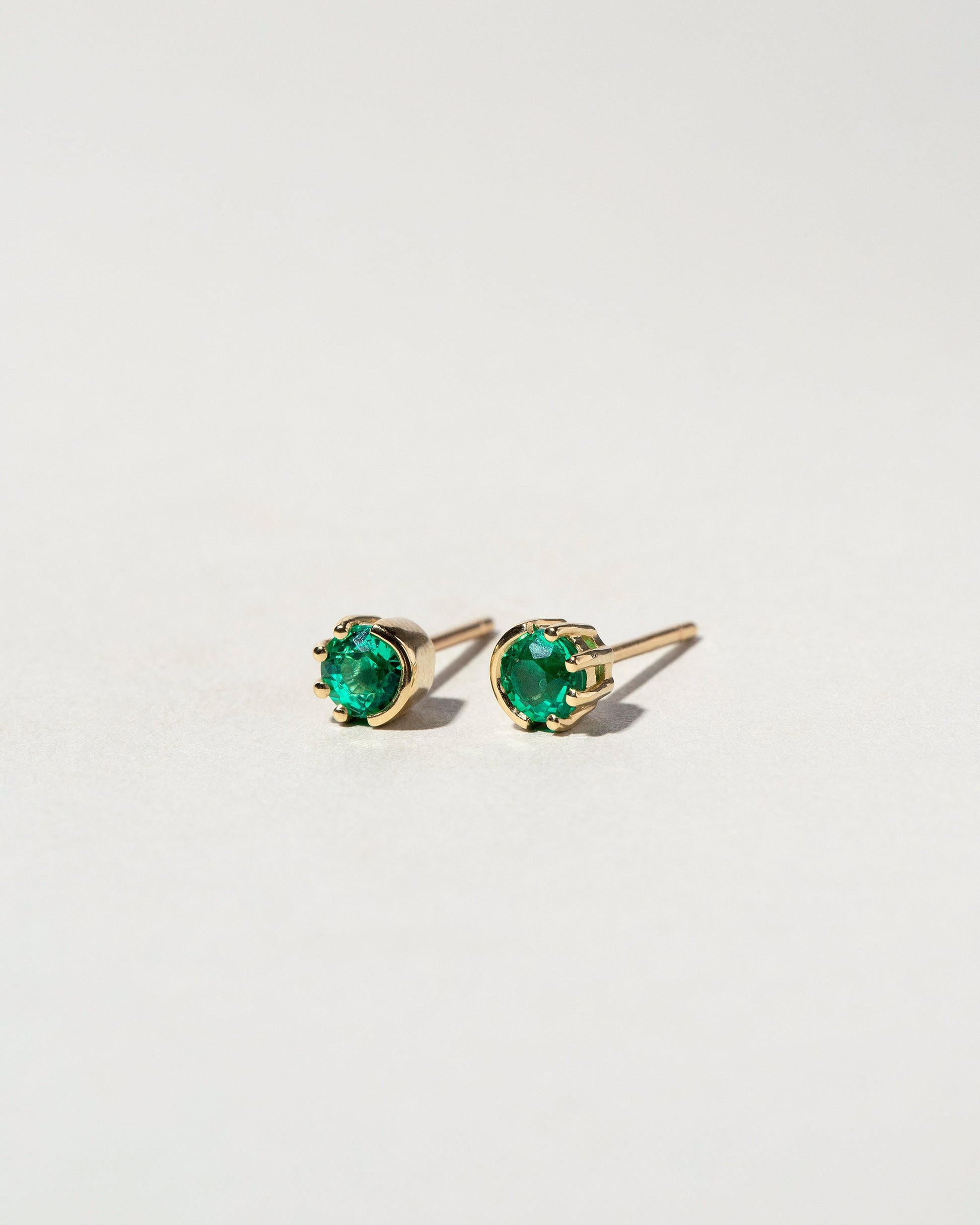 Emerald Sun & Moon Stud Earrings on light color background.