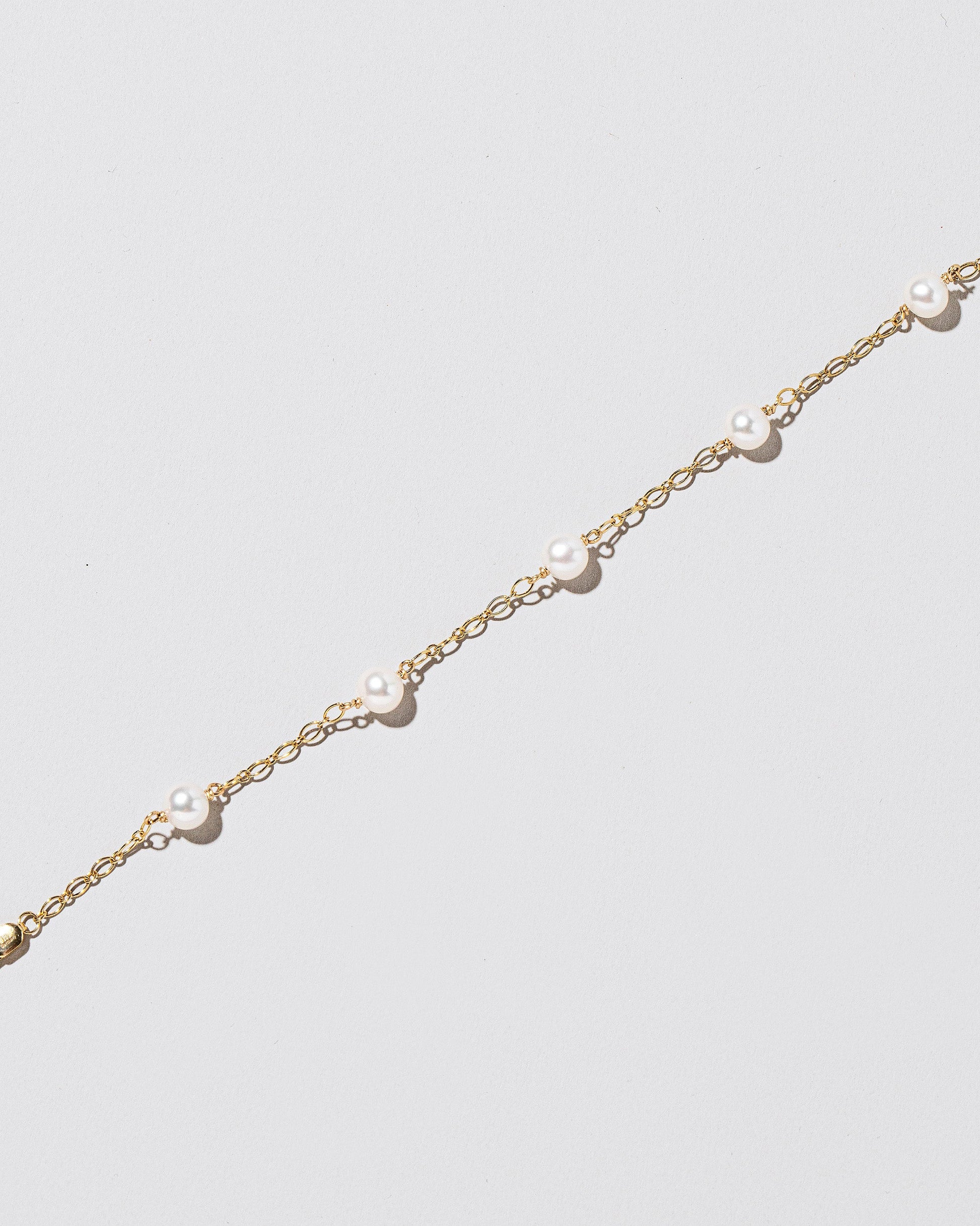 Closeup details of the Five Pearl Station Bracelet Open Oval Chain on light color background.