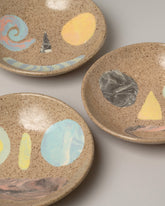 Closeup details of a group of E.E. Ceramics Speckle Smiley Bowls on light color background.