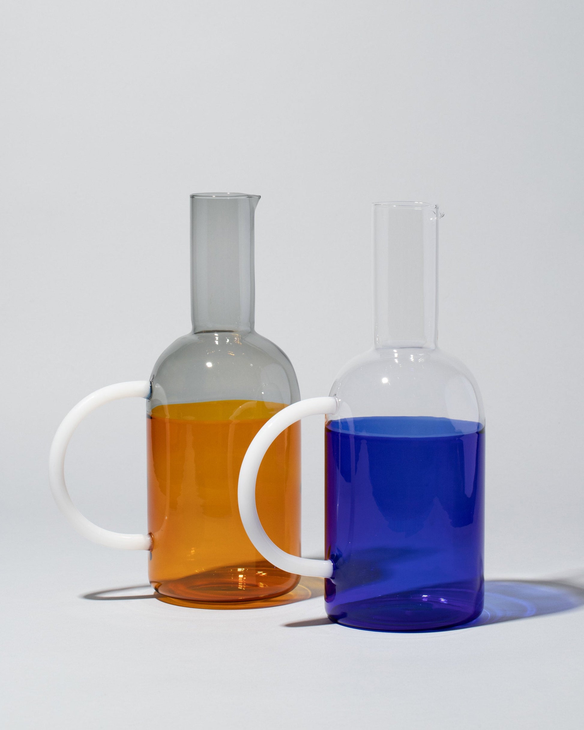 Group of Ichendorf Milano Amber/Smoke and Blue/Clear Tequila Sunrise Jugs on light color background.