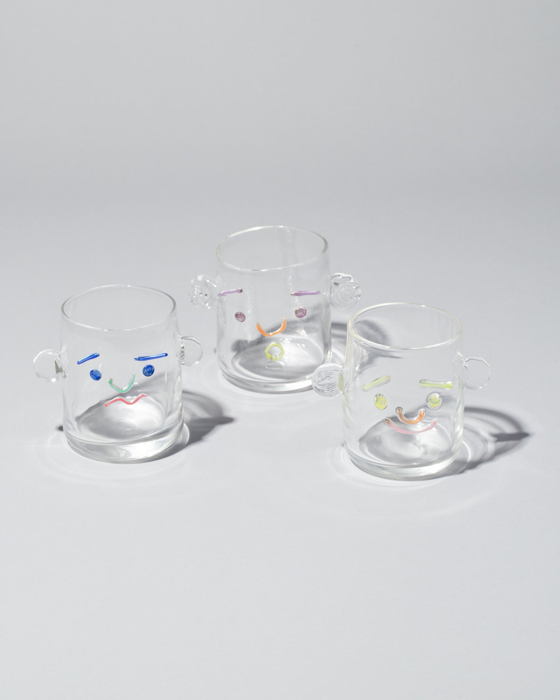 Group of TAK TAK Goods Salty, Surprised and Smiley Face Cups on light color background.