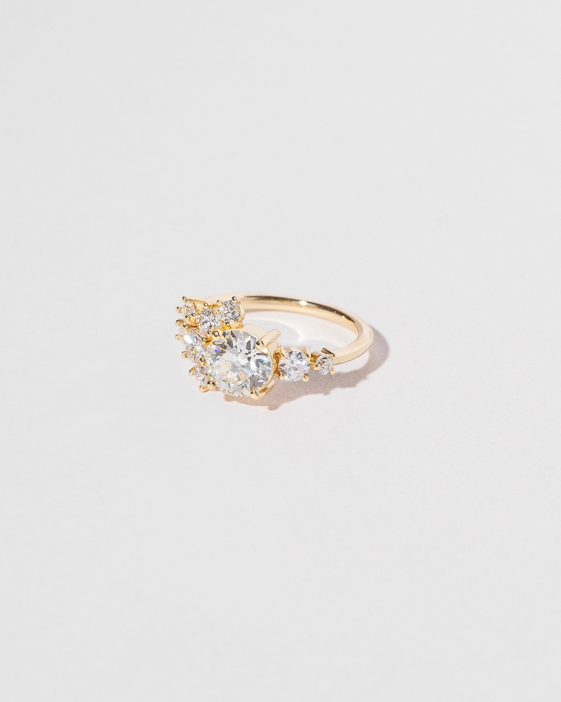 Cluster style ring with white diamonds set in 18k yellow gold, right side close up on light color background.